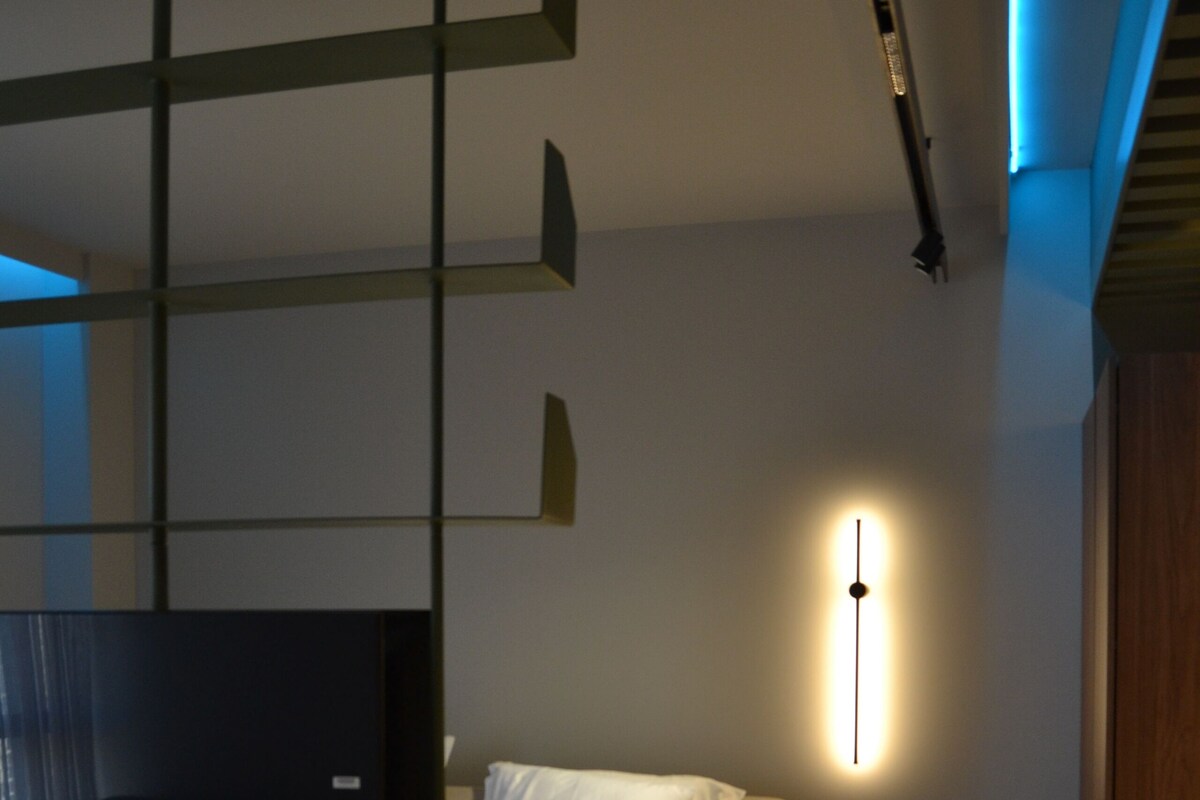 Ein modernes Hotelzimmer mit Bett, Schreibtisch, Stuhl, Fernseher und Wandleuchte.
