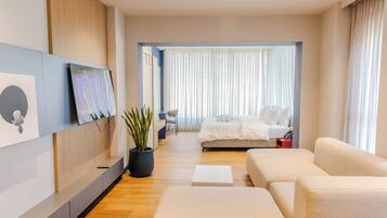 Habitación de hotel moderna con cama, sofá, televisor montado en la pared y planta en maceta.