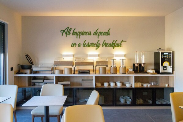 A modern breakfast area with a wall sign, seating, and kitchen appliances. - Si Hotel Sh.p.k (Tirana)