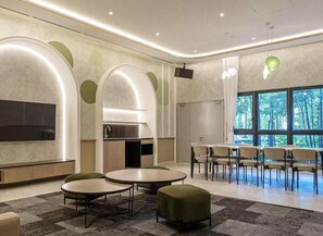 Ein modernes Interieur mit runden Tischen, grünen Sitzgelegenheiten, einem Flachbildfernseher und großen Fenstern.