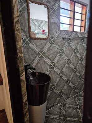 Une salle de bain avec un mur décoré d’un motif imitant le marbre, un miroir, une fenêtre et une poubelle.