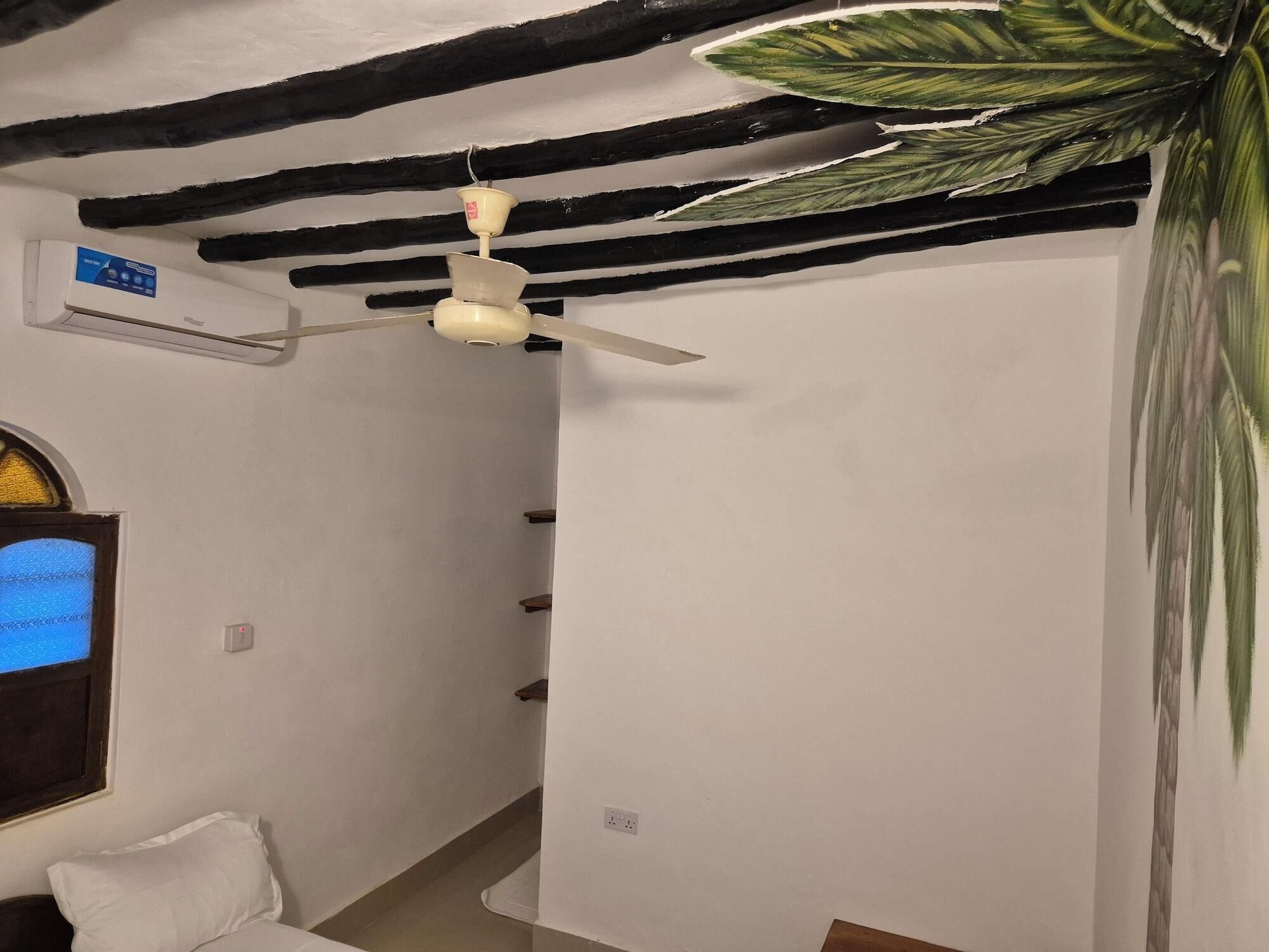 Una habitación con ventilador de techo, aire acondicionado instalado en la pared, ventana con vistas y una planta grande.