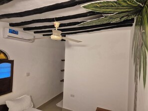 Ein Zimmer mit Deckenventilator, Wandklimaanlage, Fenster mit Aussicht und einer großen Pflanze.