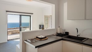 A modern kitchen with a black countertop, a sink, and a view of the sea through a large window. - Ocean Villa Paros (Paros)