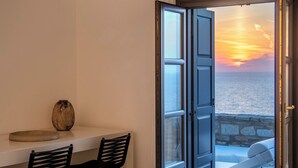 A room with a table and two chairs, a vase, and a view of the sea through an open door. - Ocean Villa Paros (Paros)