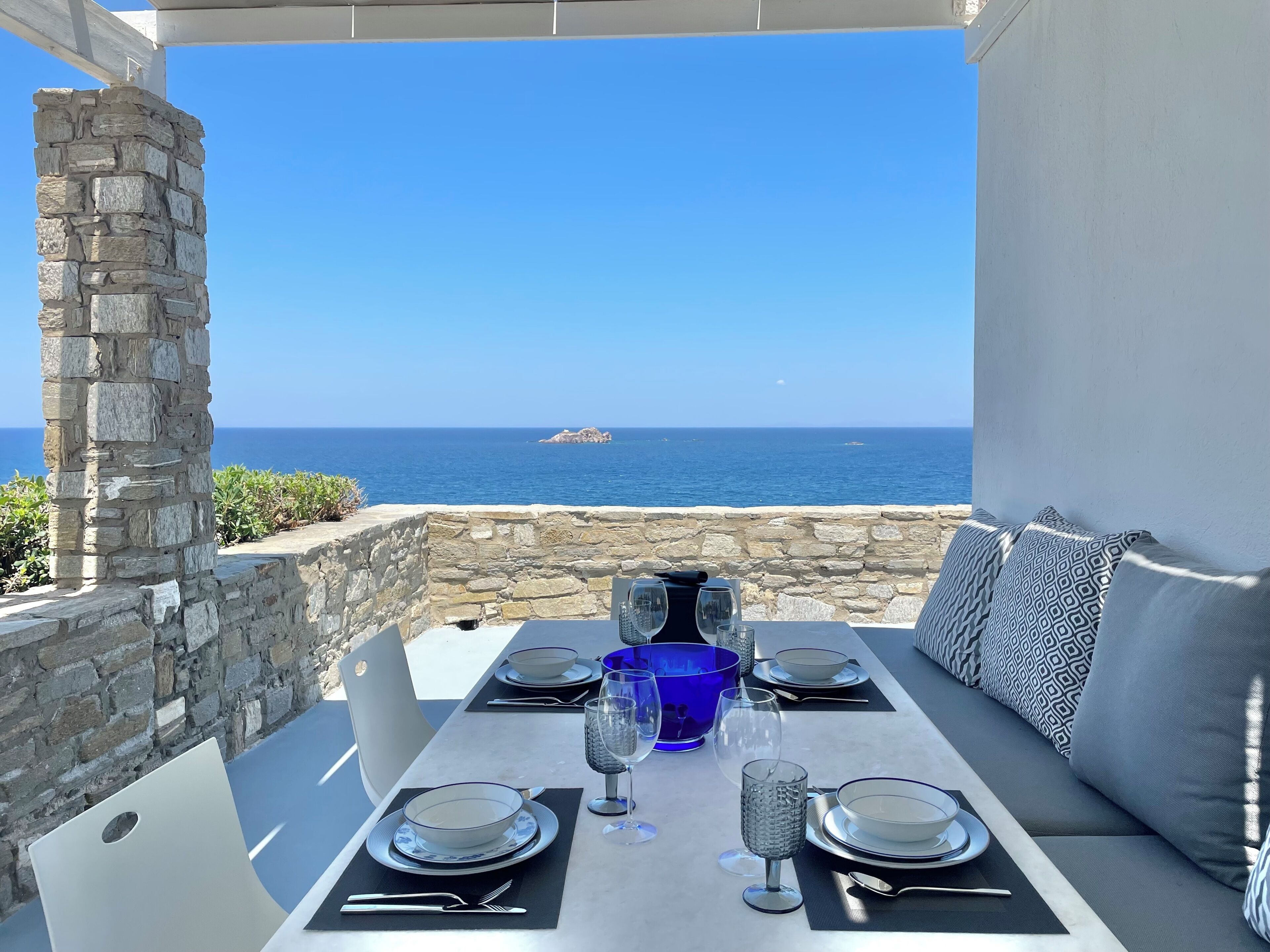 A table set for dining with a view of the sea, stone walls, and a stone pillar.