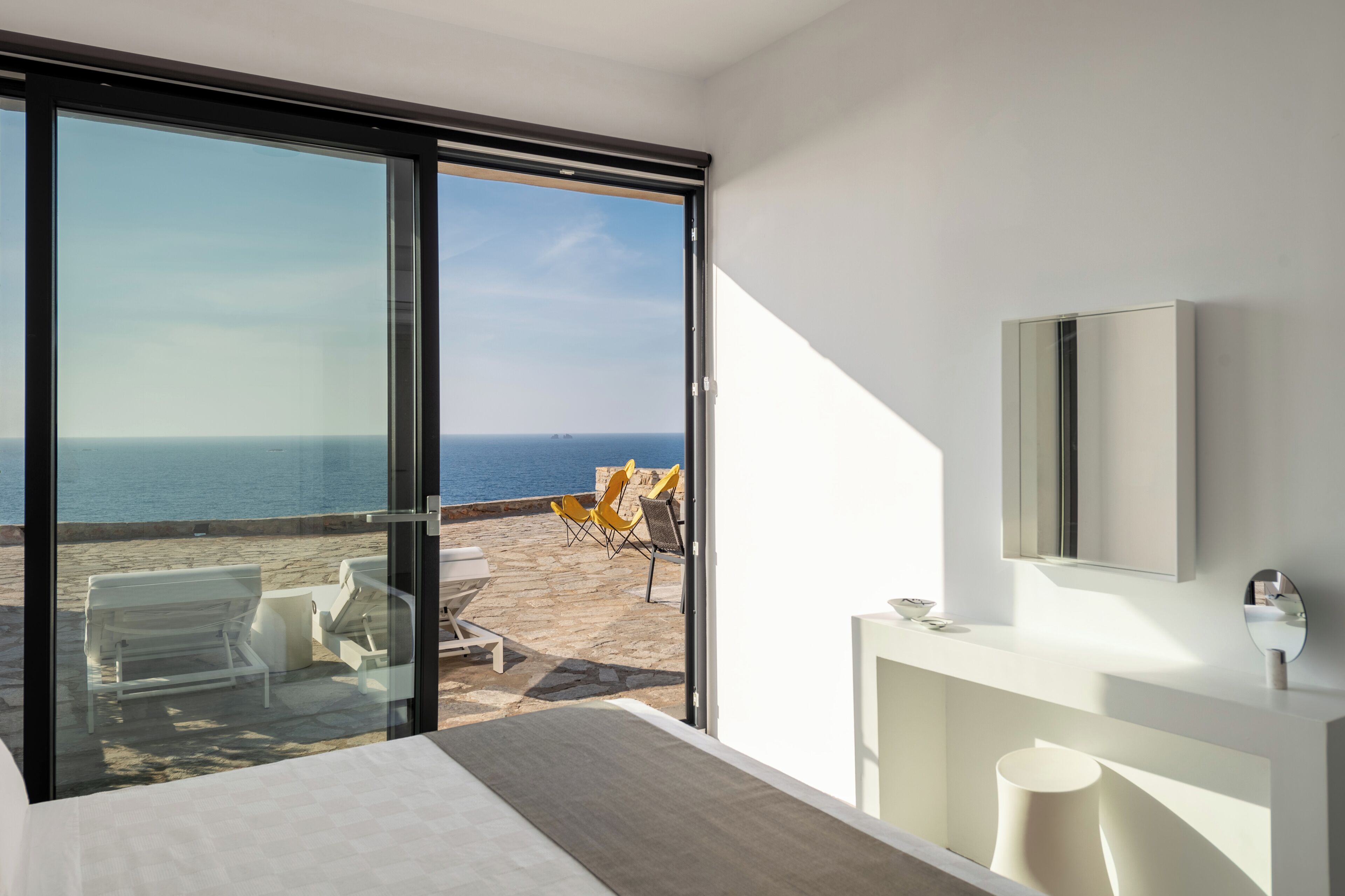 A modern hotel room with a large sliding glass door leading to a balcony with a view of the sea.