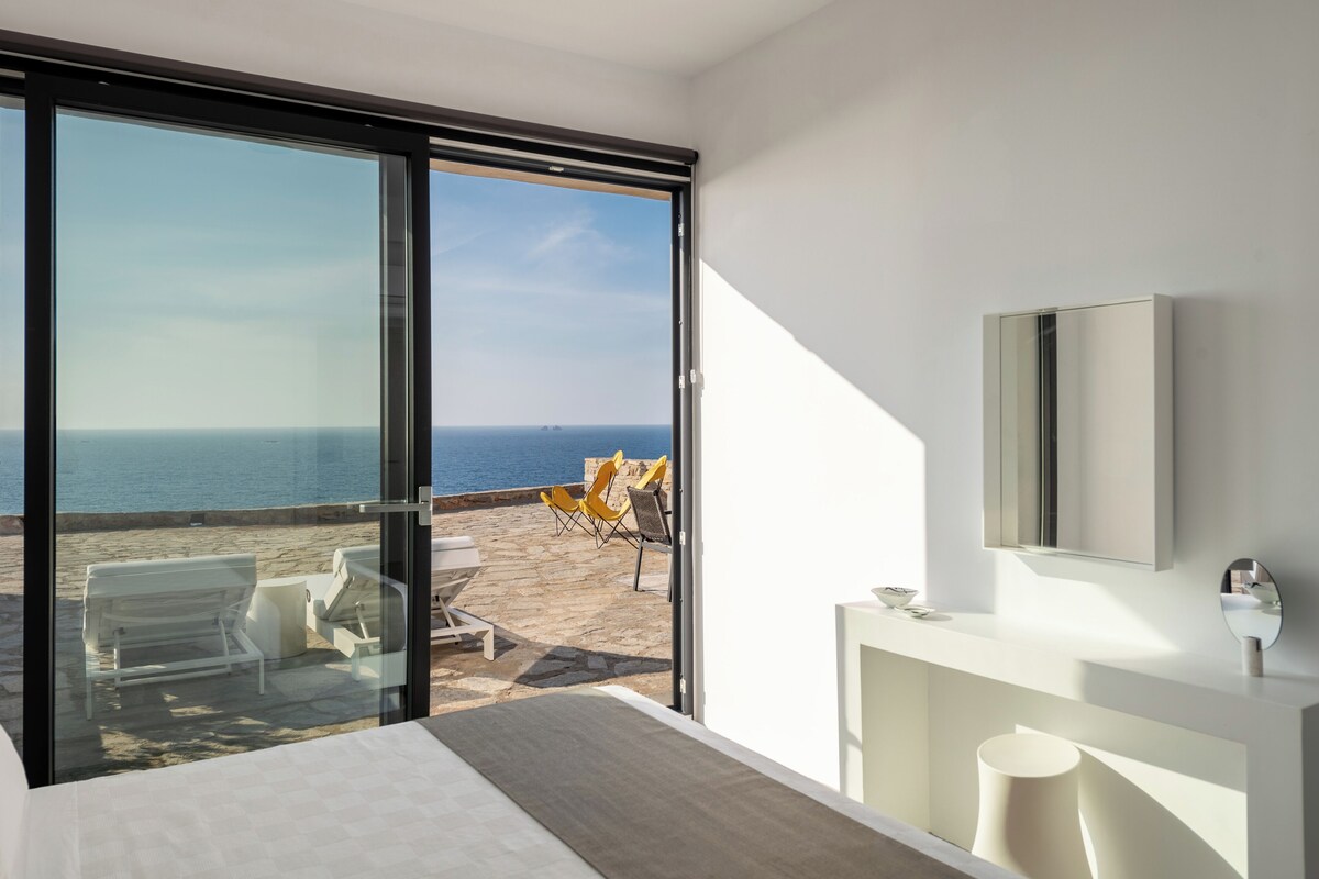 Ein modernes Hotelzimmer mit einer großen Schiebeglas-Tür, die auf einen Balkon mit Meerblick führt.