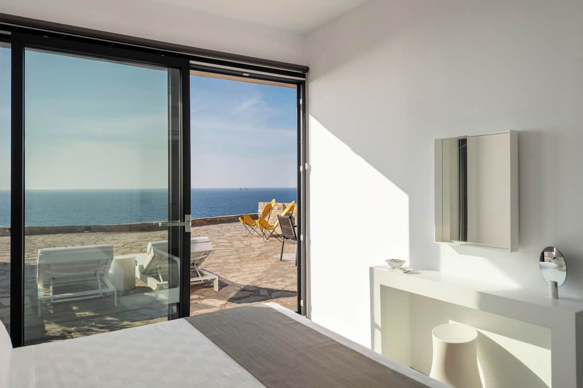 Ein modernes Hotelzimmer mit einer großen Schiebeglas-Tür, die auf einen Balkon mit Meerblick führt.