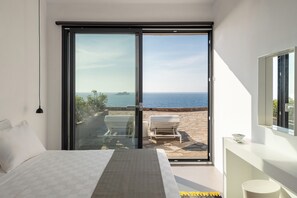 Ein Schlafzimmer mit einem Bett und einer Glastür, die zu einem Außenbereich mit Meerblick führt.