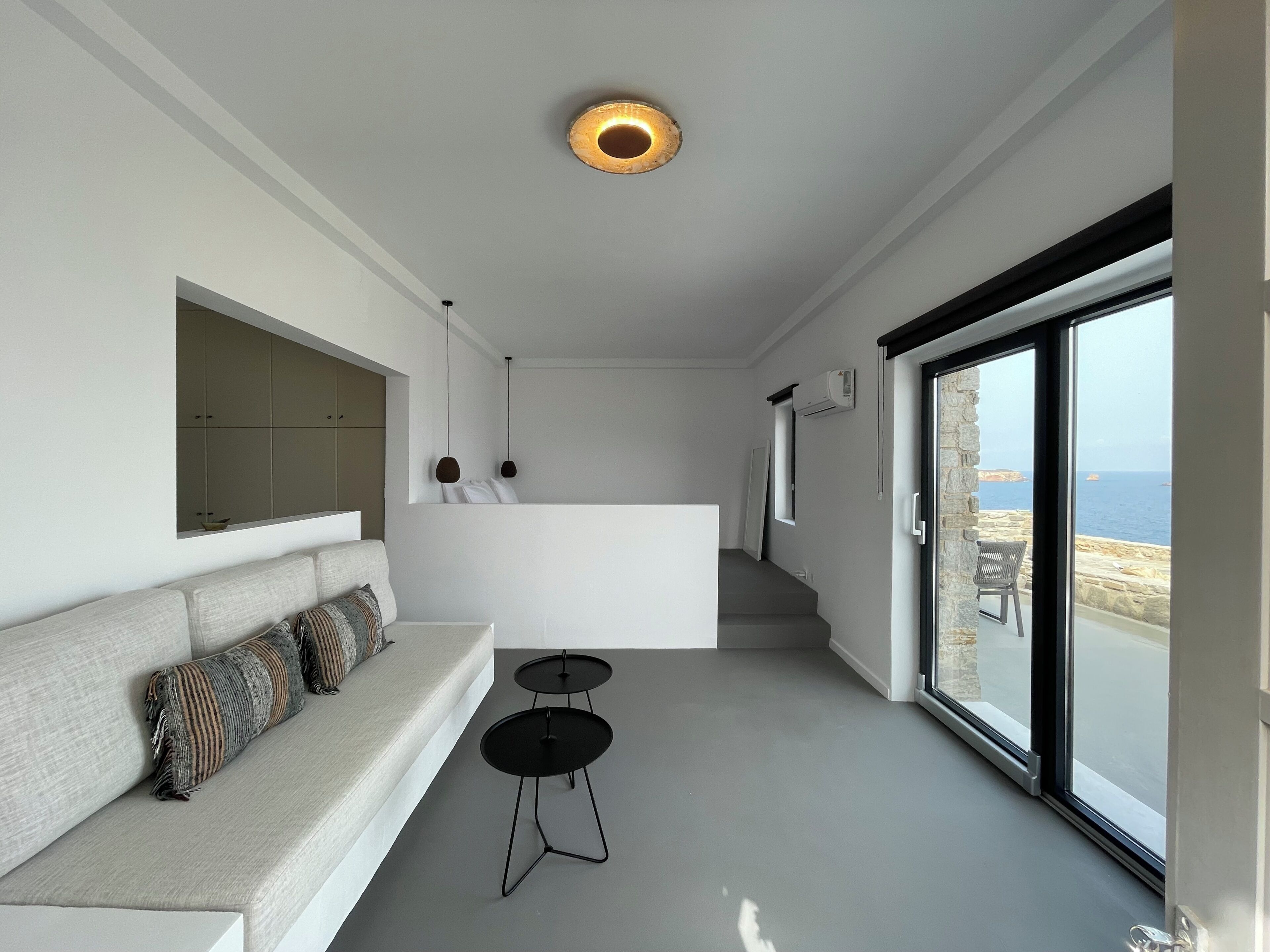 A modern interior with a sofa, a small table, a mirror, and a view of the sea.