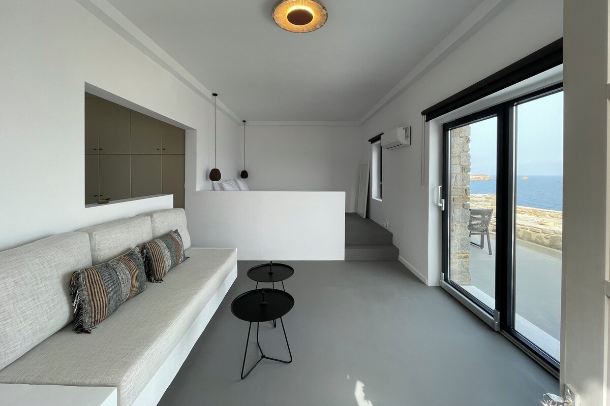 Ein modernes Interieur mit einer Couch, einem kleinen Tisch, einem Spiegel und Meerblick durch große Fenster.