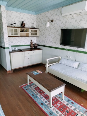 A room with a sofa, a coffee table, a cabinet, a television, and a patterned rug. - Yeşil Ev Butik Otel & Kafe (Gökçeada)