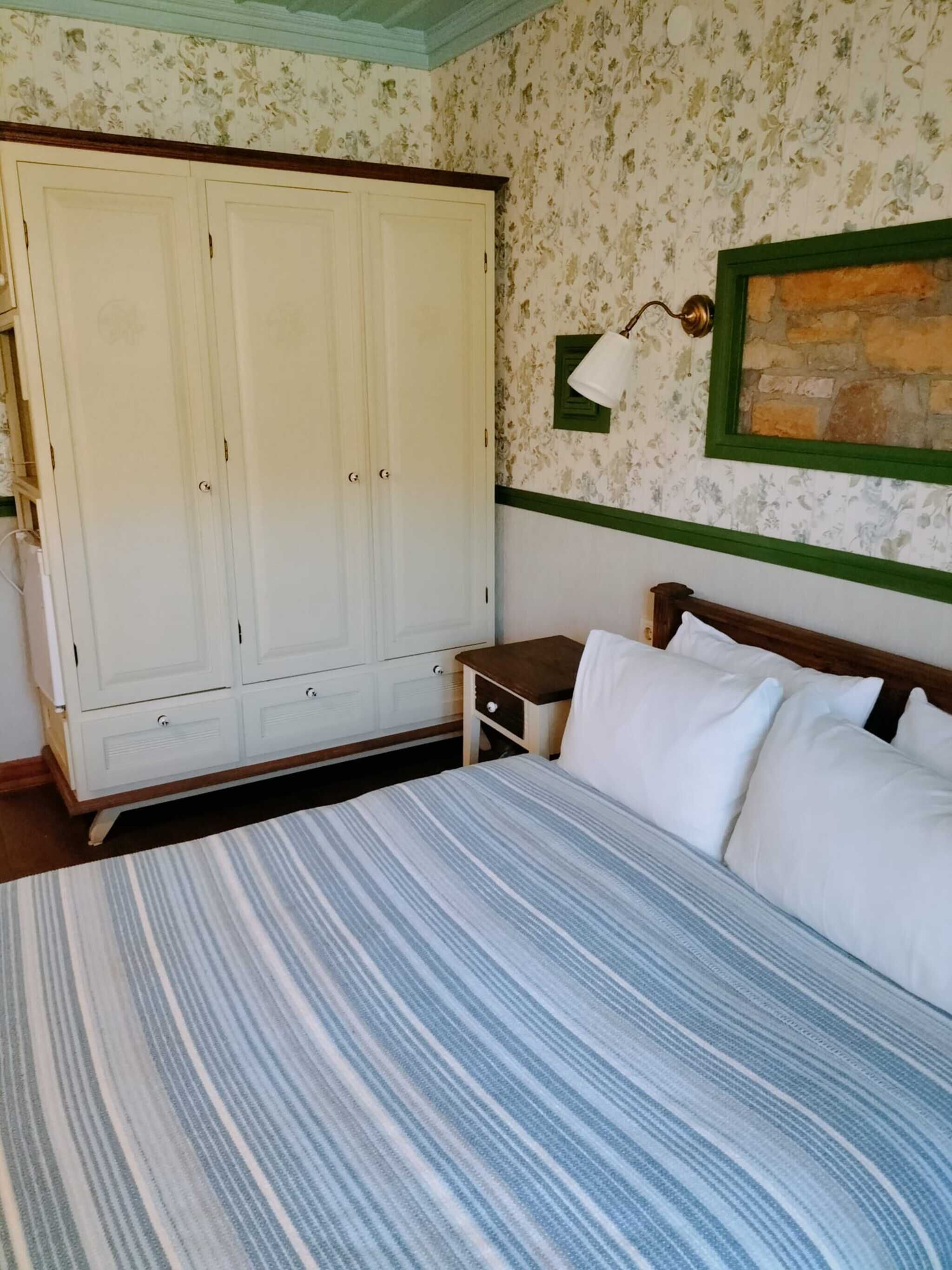 A bedroom with a bed, a wardrobe, a nightstand, and a wall-mounted lamp.