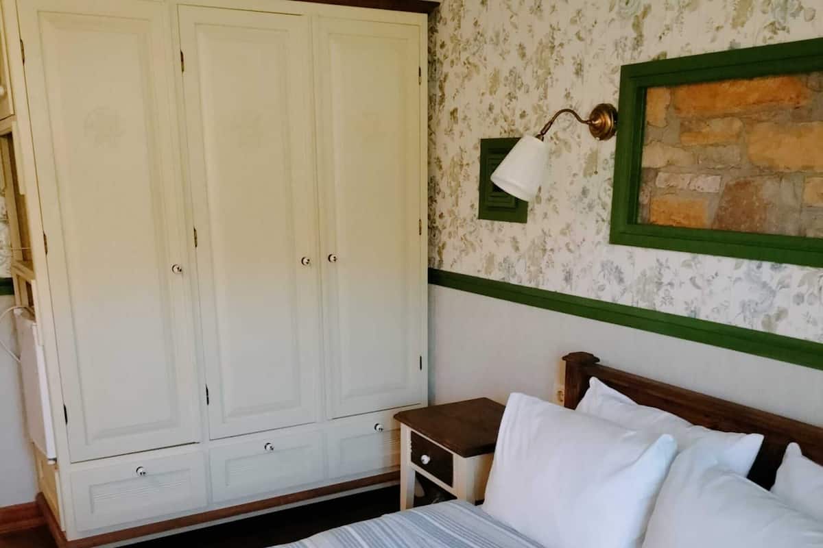 A bedroom with a bed, a wardrobe, a nightstand, and a wall-mounted lamp.