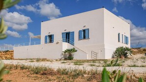 Edifici blanc amb persianes blaves, una escala i un balcó.