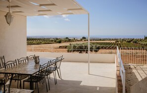Eine Terrasse im Freien mit Tisch und Stühlen, einer Pergola und Blick auf Weinberge und ferne Hügel.