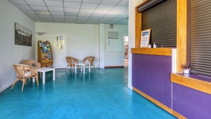 Un área de recepción con mostrador, dos sillones de mimbre, una mesita y un panel decorativo en la pared.