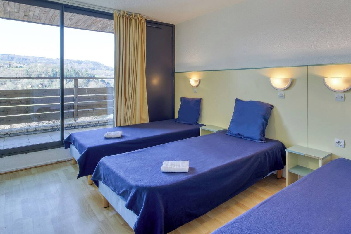A hotel room with two beds, a window with curtains, and a balcony with a view.