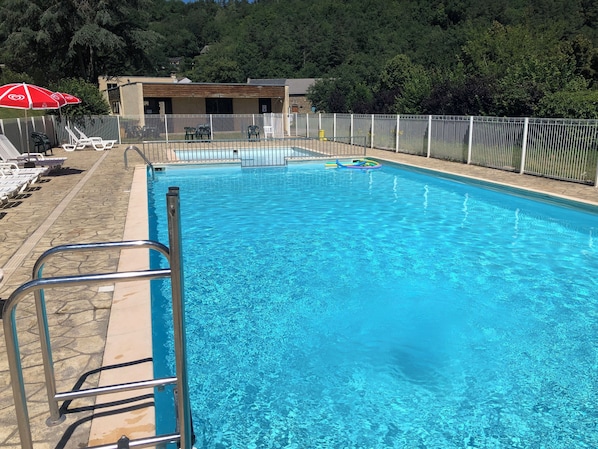 A swimming pool with a metal ladder, lounge chairs, and a fenced area.