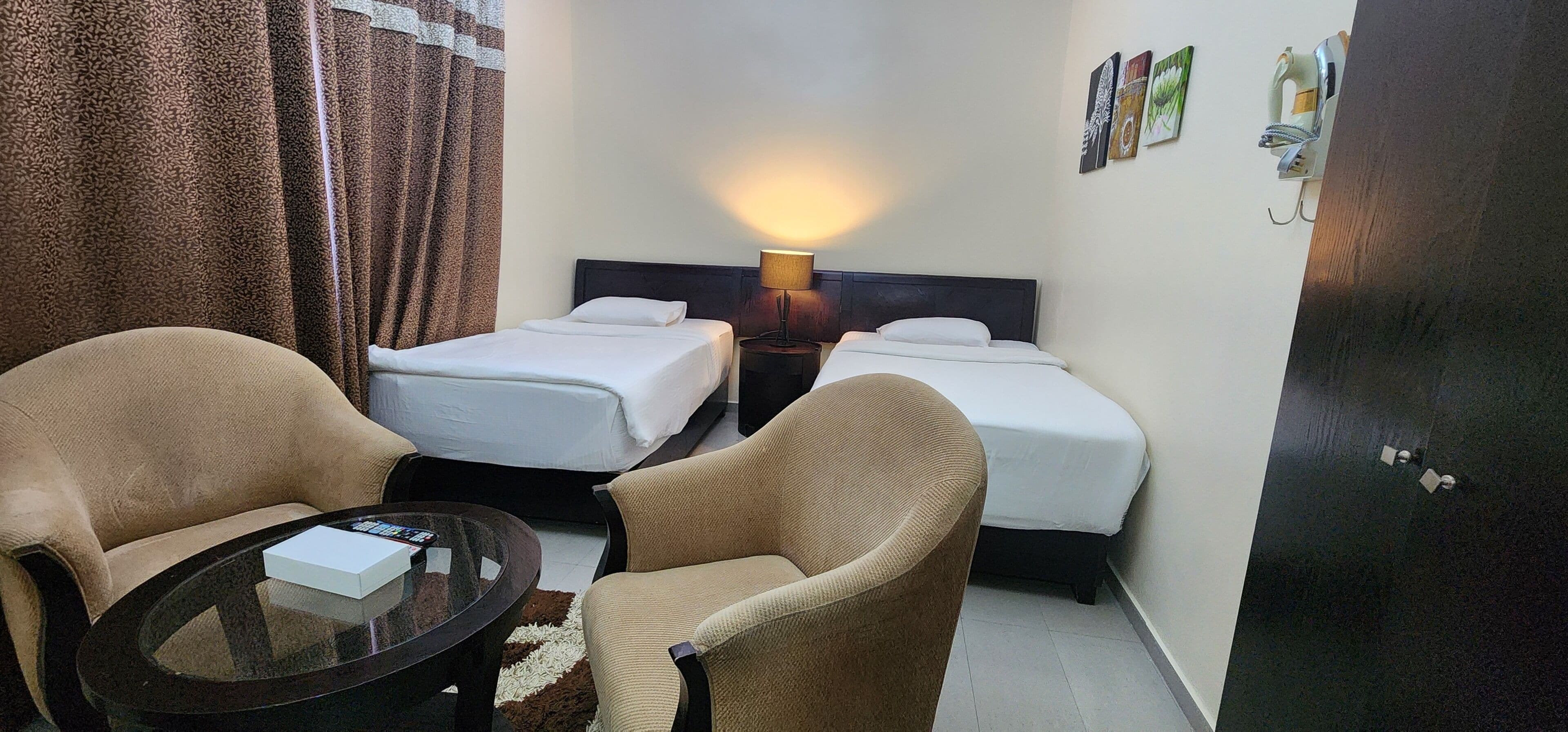 A hotel room with two single beds, a sofa, a small table, and a lamp.