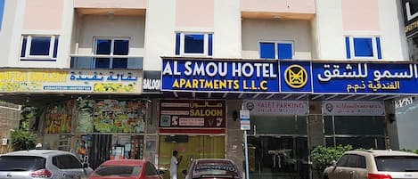 Un hotel de varios pisos con balcones, una zona de estacionamiento y diversos comercios.