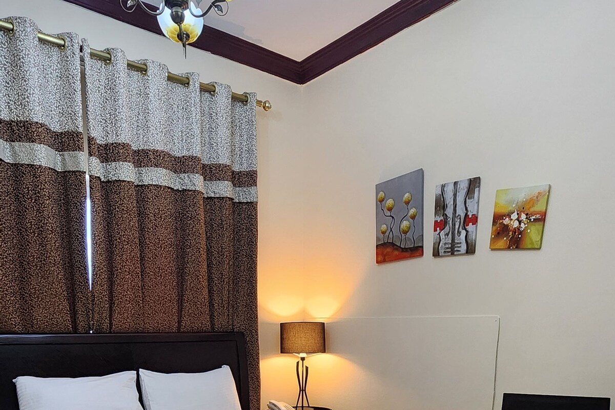 Una habitación de hotel con una cama, una mesita de noche, una lámpara y una obra de arte en la pared.