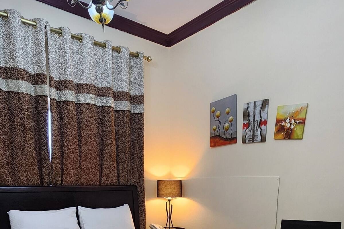 A hotel room with a bed, a bedside table, a lamp, and artwork on the wall.