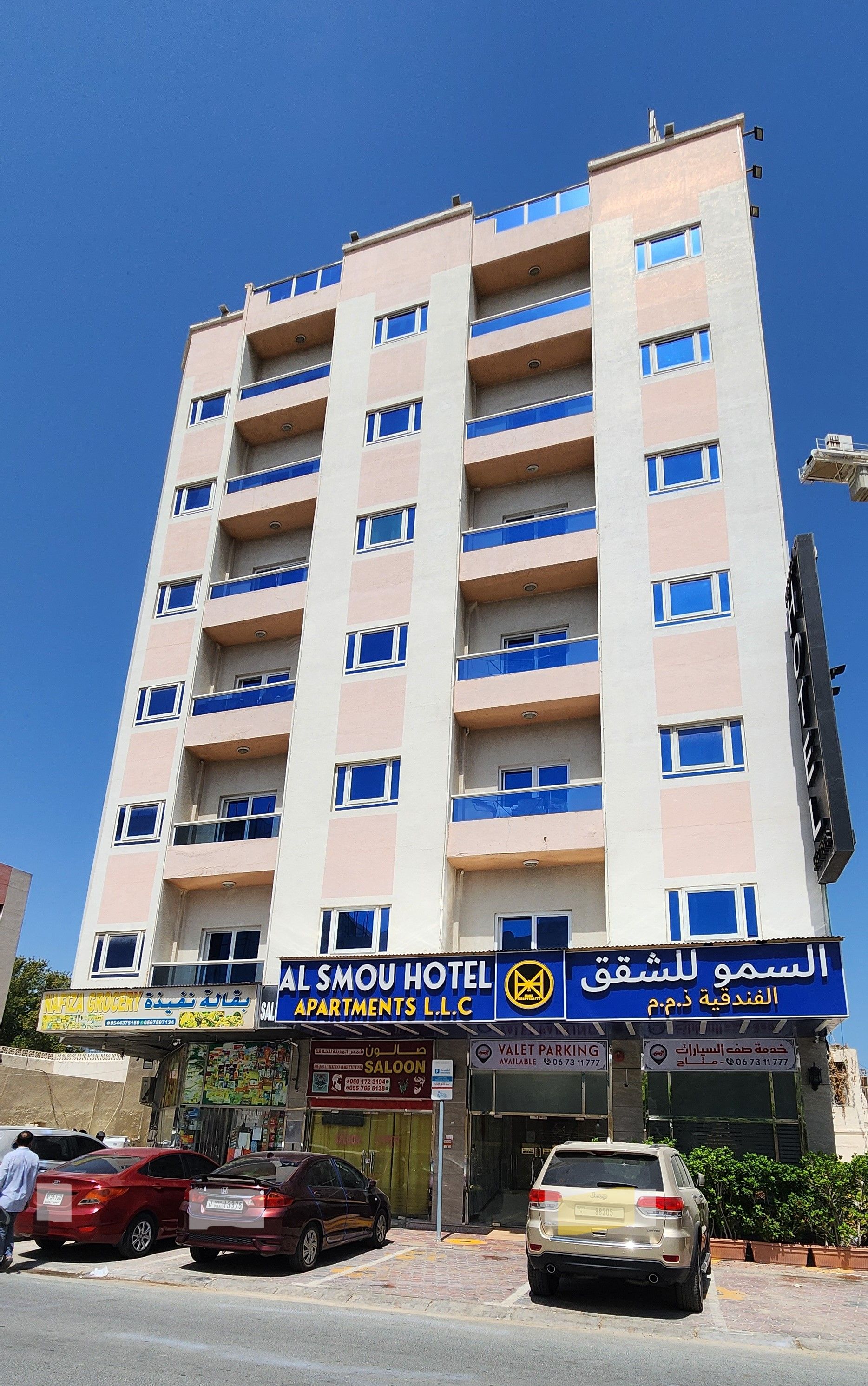 A multi-story hotel with balconies, a sign for 'AL SMOU HOTEL,' and a 'VALET PARKING' sign.