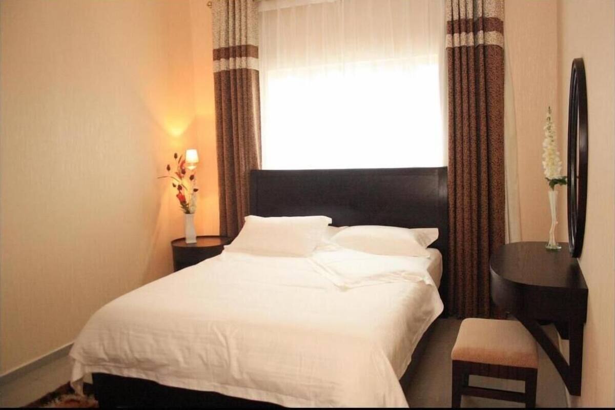 A hotel room with a bed, bedside table, lamp, and a mirror.