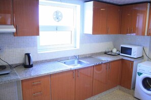 Una cocina con armarios de madera, un fregadero, un microondas, una tetera y una lavadora.