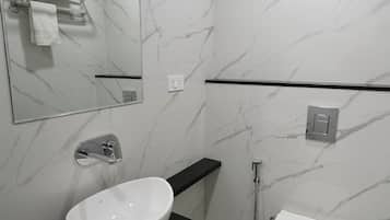 A modern bathroom with a white marble wall, a black countertop, a white sink, a toilet, a mirror, and a shower.