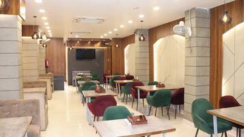 A modern restaurant interior with multiple tables and chairs, a flat-screen TV mounted on the wall, and recessed ceiling lighting.