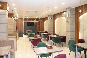 Ein modernes Restaurant mit mehreren Tischen und Stühlen, einem an der Wand befestigten Flachbildfernseher und Einbaustrahler.