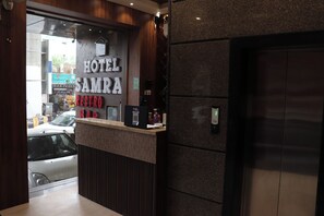 A hotel reception desk with a sign reading 'HOTEL SAMRA,' a counter with a computer, and an elevator. - Hotel Samrat Ajmer (Ajmer)