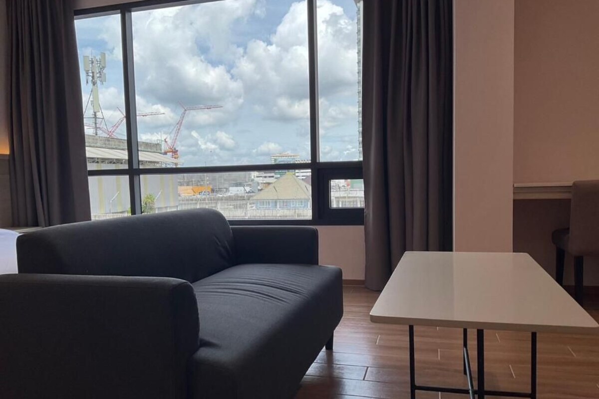 Quarto com sofá, mesa e uma grande janela com vista para um canteiro de obras.