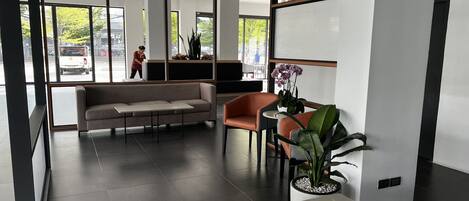 A modern lobby with a sofa, chairs, a table, and potted plants.