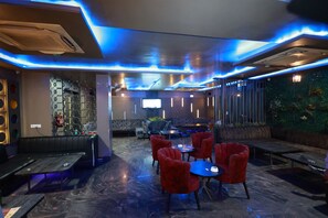 A modern interior with a bar area, seating with red chairs, and a television screen.
