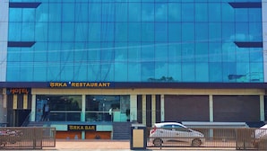 Un edificio moderno con fachada de vidrio, que muestra un letrero que indica 'Hotel Jai Harsh & Bar' y 'Restaurante Orka'.