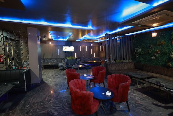 A modern lounge area with a bar, red upholstered chairs, and a television.