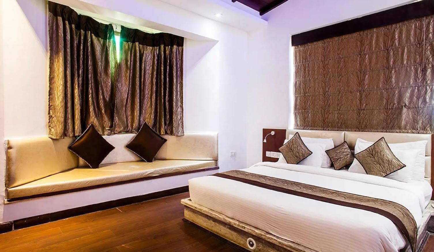 A hotel room with a bed, a sofa, and a window with curtains.