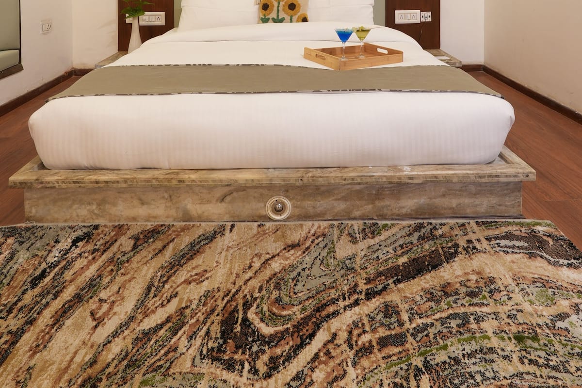 A bedroom with a large bed, a wooden headboard, a window with blinds, a bedside table with a lamp, and a wall-mounted air conditioner.