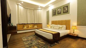 A modern hotel room with a large bed, a sofa bed, a flat-screen TV, a window with curtains, and framed pictures on the wall.