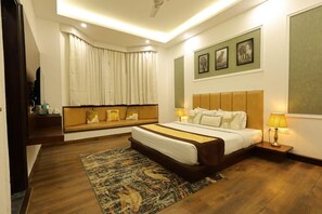 Una habitación de hotel moderna con una cama grande, un sofá cama, un televisor de pantalla plana, una ventana con cortinas y cuadros enmarcados en la pared.