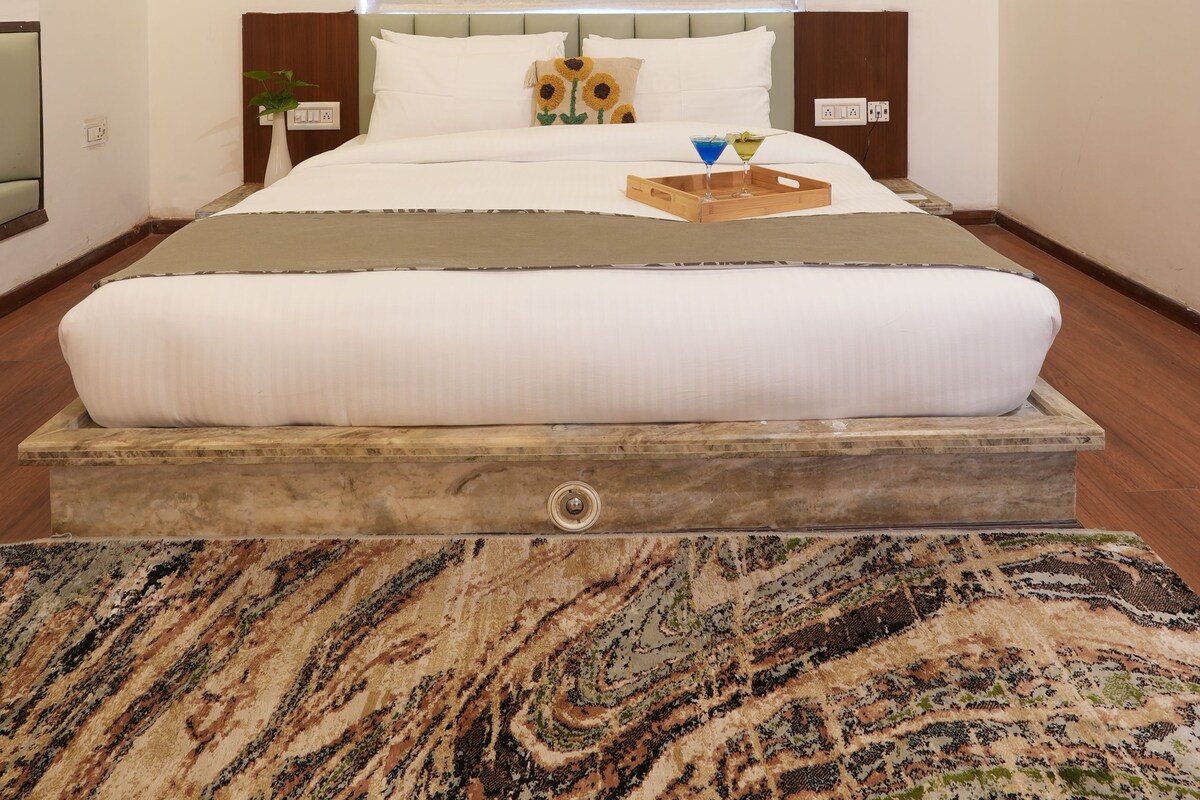 Un dormitorio con una cama grande, cabecera de madera, ventana con persianas, mesita de noche con lámpara y aire acondicionado instalado en la pared.