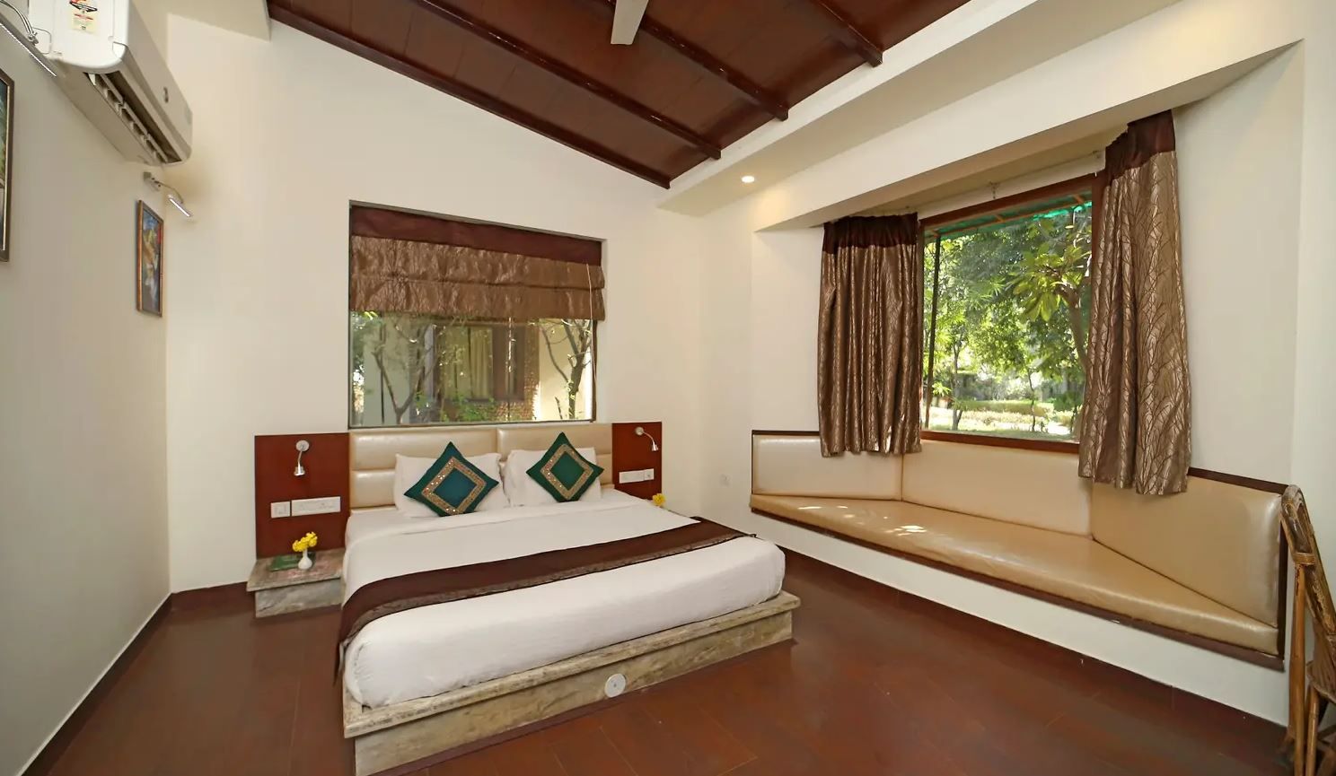 A bedroom with a bed, a bench, a window with curtains, and an air conditioning unit.