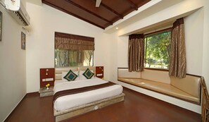 Un dormitorio con cama, una banca, ventana con cortinas y un equipo de aire acondicionado.