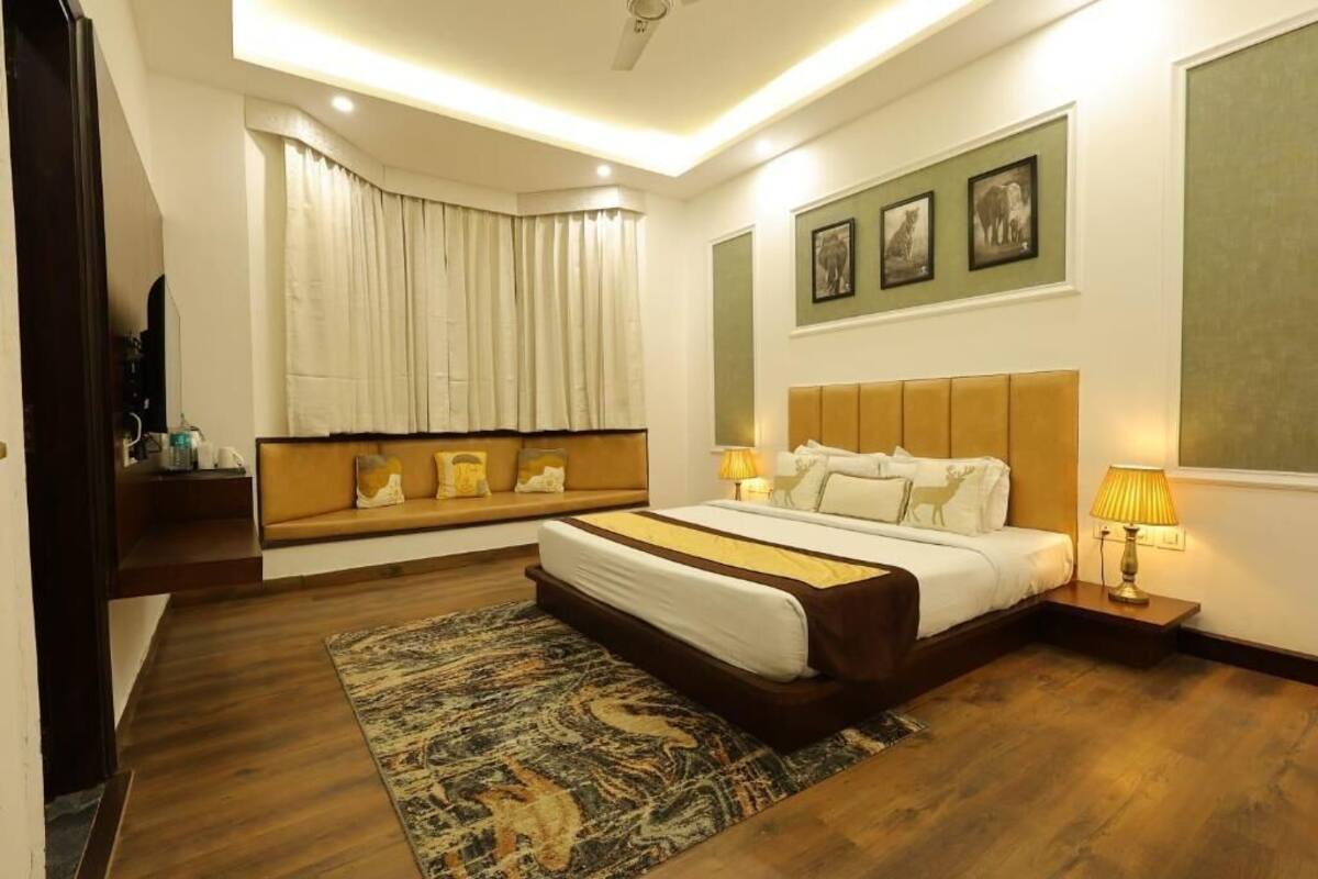 Una habitación de hotel moderna con una cama grande, un sofá cama, un televisor de pantalla plana, una ventana con cortinas y cuadros enmarcados en la pared.