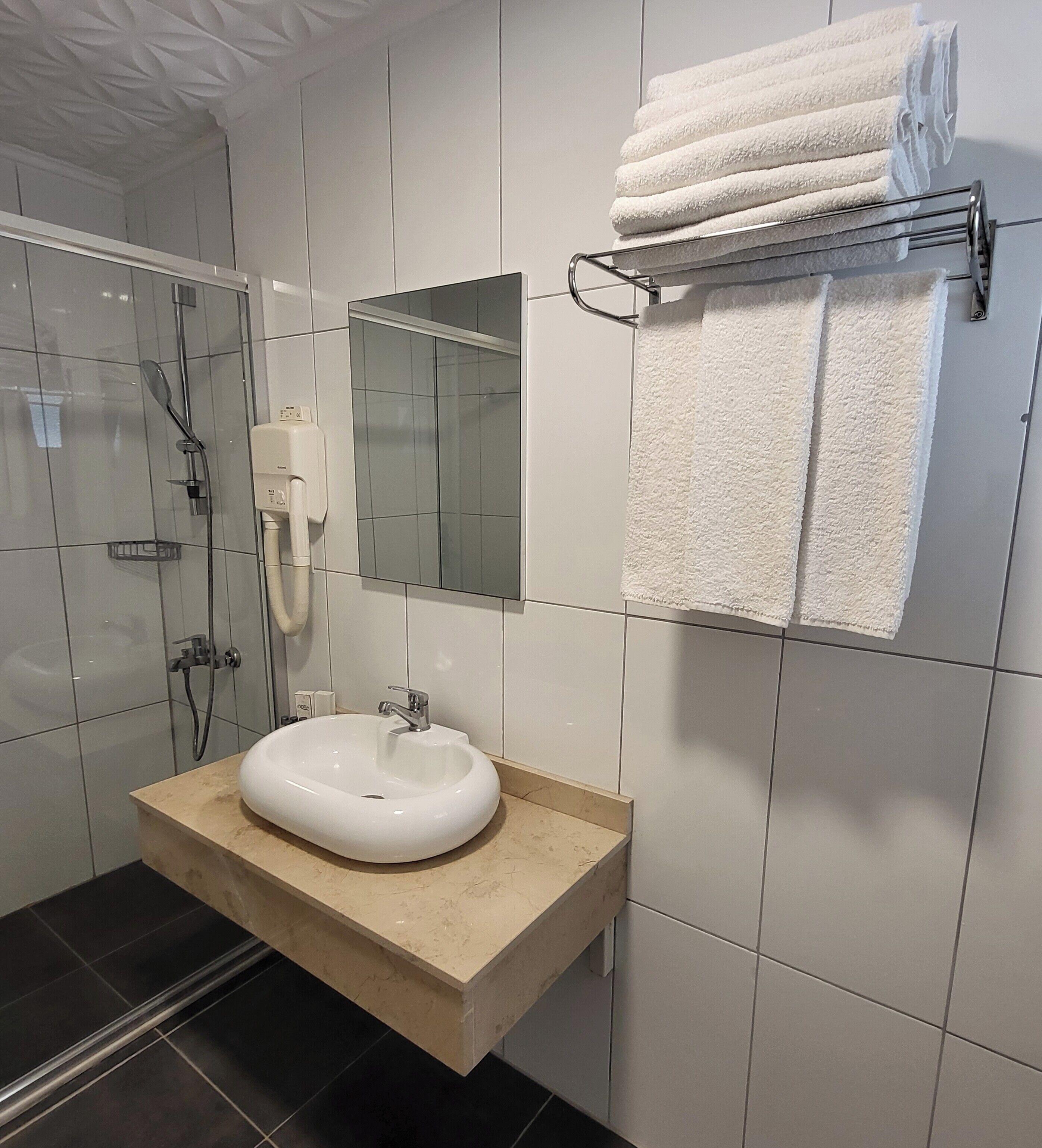 A modern bathroom with a glass shower enclosure, a white sink, and a towel rack.