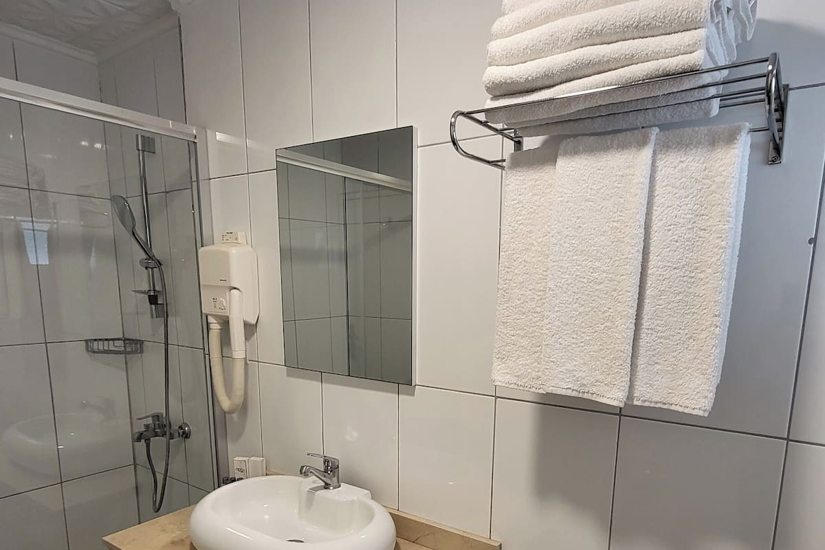 Moderni kylpyhuone, jossa on lasinen suihkuseinä, valkoinen pesuallas ja pyyhekoukku.